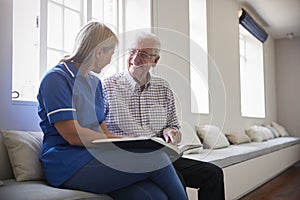 Senior man sitting looking at photo album with care nurse