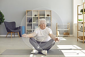 Senior man sitting in lotus position on fitness mat and meditating with eyes closed