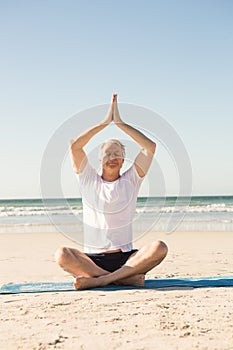 Senior man sitting on mat while meditating at beach
