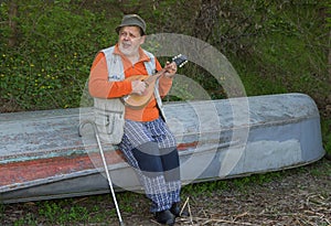Senior man sitting on an old reversed boat and singing