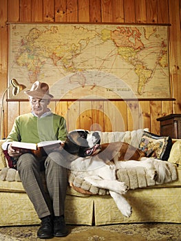 Senior man sitting on sofa with dog reading book