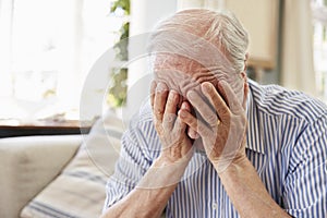 Senior Man Sitting On Sofa At Home Suffering From Depression