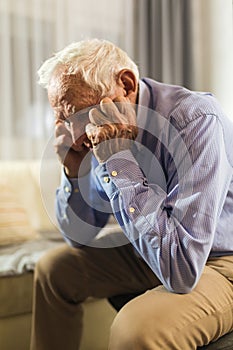 Senior Man Sitting On Sofa Suffering From Depression