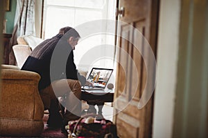 Senior man sitting on sofa using laptop having video call