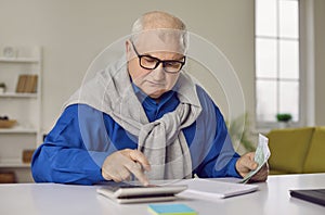 Senior man sitting at the table and calculating finances or taxes at home.