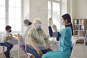 Senior man sitting at table at the hospital and watching nurse getting flu shot ready