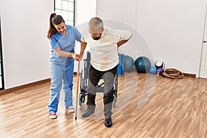 Senior man sitting on wheelchair being assited by geriatric nurse, handicapped mature man getting help to stand up