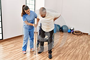 Senior man sitting on wheelchair being assited by geriatric nurse, handicapped mature man getting help to stand up