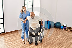 Senior man sitting on wheelchair being assited by geriatric nurse, handicapped mature man getting help to stand up