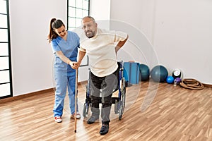 Senior man sitting on wheelchair being assited by geriatric nurse, handicapped mature man getting help to stand up