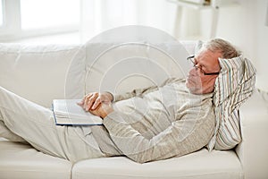 Senior man sleeping on sofa with book at home