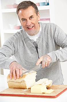 Senior Man Slicing Bread In Kitchen photo