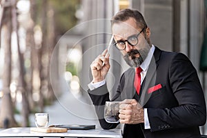 Senior man in smart business suit thinking and sitting in outdoor coffee table