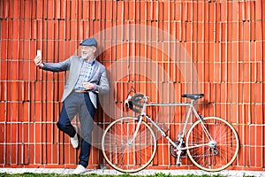 Senior man with smartphone and bicycle against brick wall.