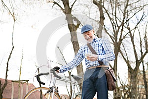 Senior man with smartphone and bicycle in town.