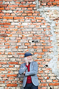 Senior man with smartphone making phone call against brick wall.