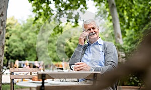Senior man with smartphone sitting outdoors in cafe, making phone call.