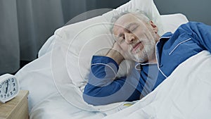 Senior man smiling while asleep in the morning, pleased pensioner lying in bed