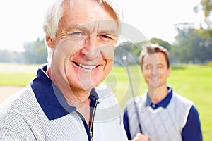 Senior man smiling. Closeup of senior man smiling with son holding a golf club in background.