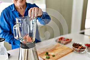 Senior man smiling confident putting datil in blender at kitchen