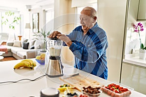 Senior man smiling confident shaking blender at kitchen