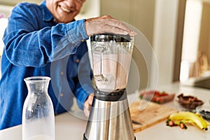 Senior man smiling confident shaking blender at kitchen