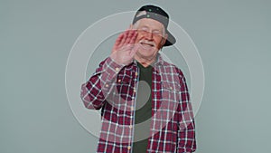 Senior man smiling friendly at camera and waving hands gesturing hello or goodbye, welcoming