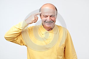 Senior man smiling pointing to head with one finger, great idea or thought