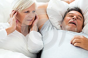 Senior man snoring and woman covering ears