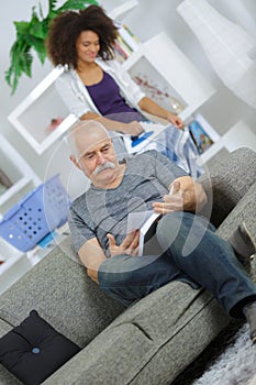 Senior man on sofa and female assistant ironing