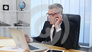 Senior man speaks with white smartphone in office