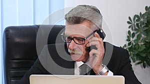 Senior man speaks with white smartphone in office