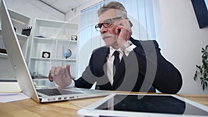 Senior man speaks with white smartphone in office