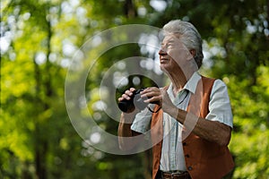 Senior man spending free time outdoors in nature, watching forest animals through binoculars.