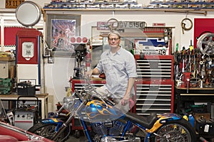 Senior man standing behind motorcycle in automobile repair shop