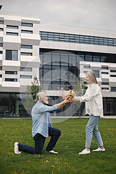 Senior man standing on a grass in summer and give straw basket to woman