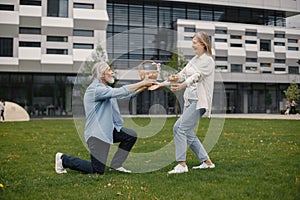 Senior man standing on a grass in summer and give straw basket to woman
