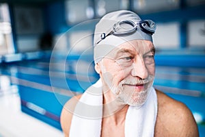 Senior man standing in an indoor swimming pool.