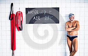 Senior man standing in an indoor swimming pool.