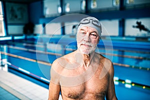 Senior man standing in an indoor swimming pool.