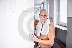 Senior man standing by the lockers in an indoor swimming pool.