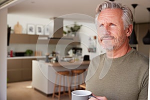Senior Man Standing And Looking Out Of Kitchen Door Drinking Coffee