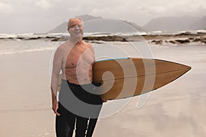 Senior man standing with surfboard on the beach