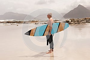 Senior man standing with surfboard on the beach