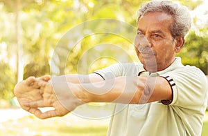 Senior man stretches hands before exercise - Concept of elderly person fitness outdoor - 60s person doing yoga asana at