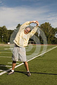 Senior man stretching exercising sports field