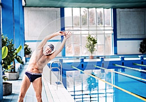 Senior man stretching by the indoor swimming pool.