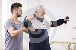 Senior man after stroke at nursing home exercising with professional physiotherapist