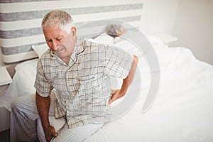 Senior man suffering from backache sitting on bed