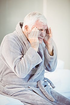 Senior man suffering from headache while sitting on bed